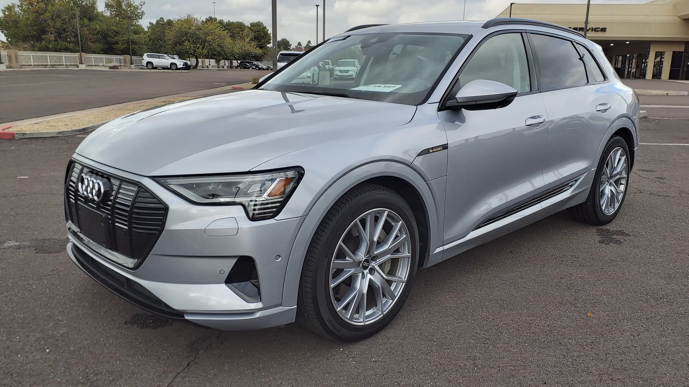 A silver Audi e-tron parked on a dealership lot under an overcast sky