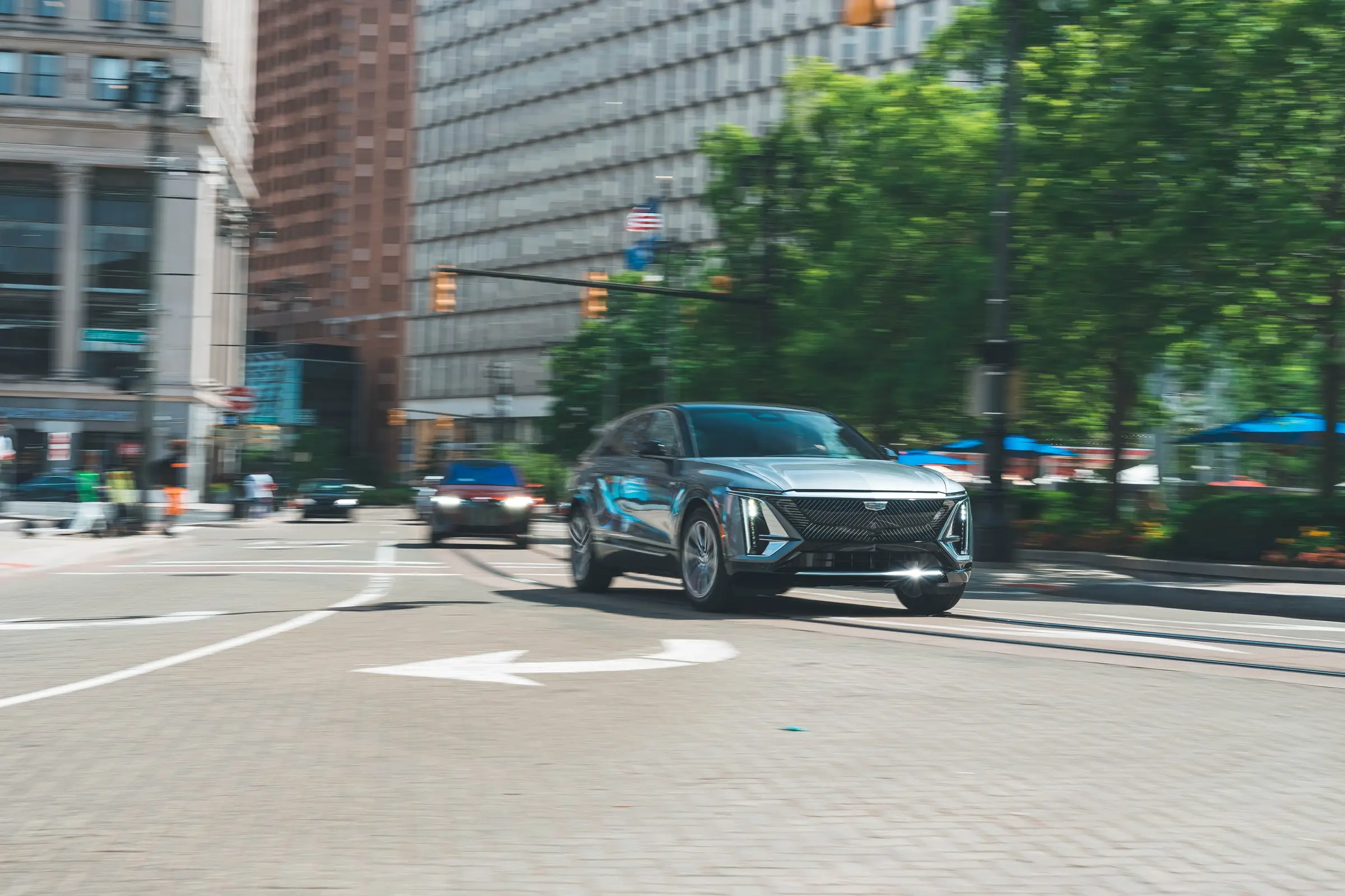 A silver Cadillac Lyriq driving through a downtown intersection