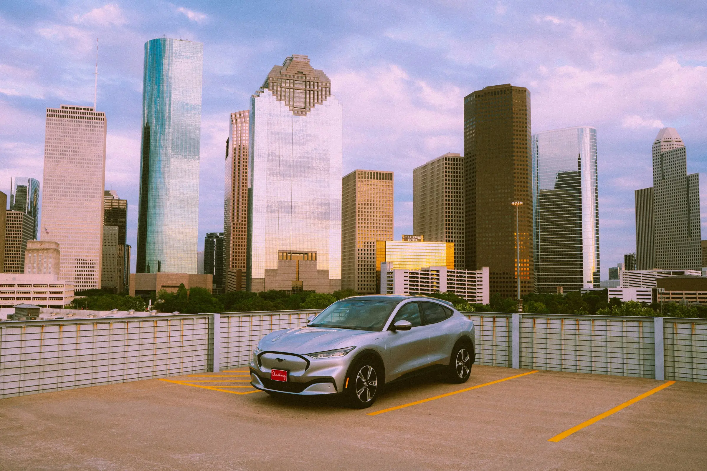 A silver Ford Mustang Mach-E parked on a rooftop lot with the Houston skyline behind it