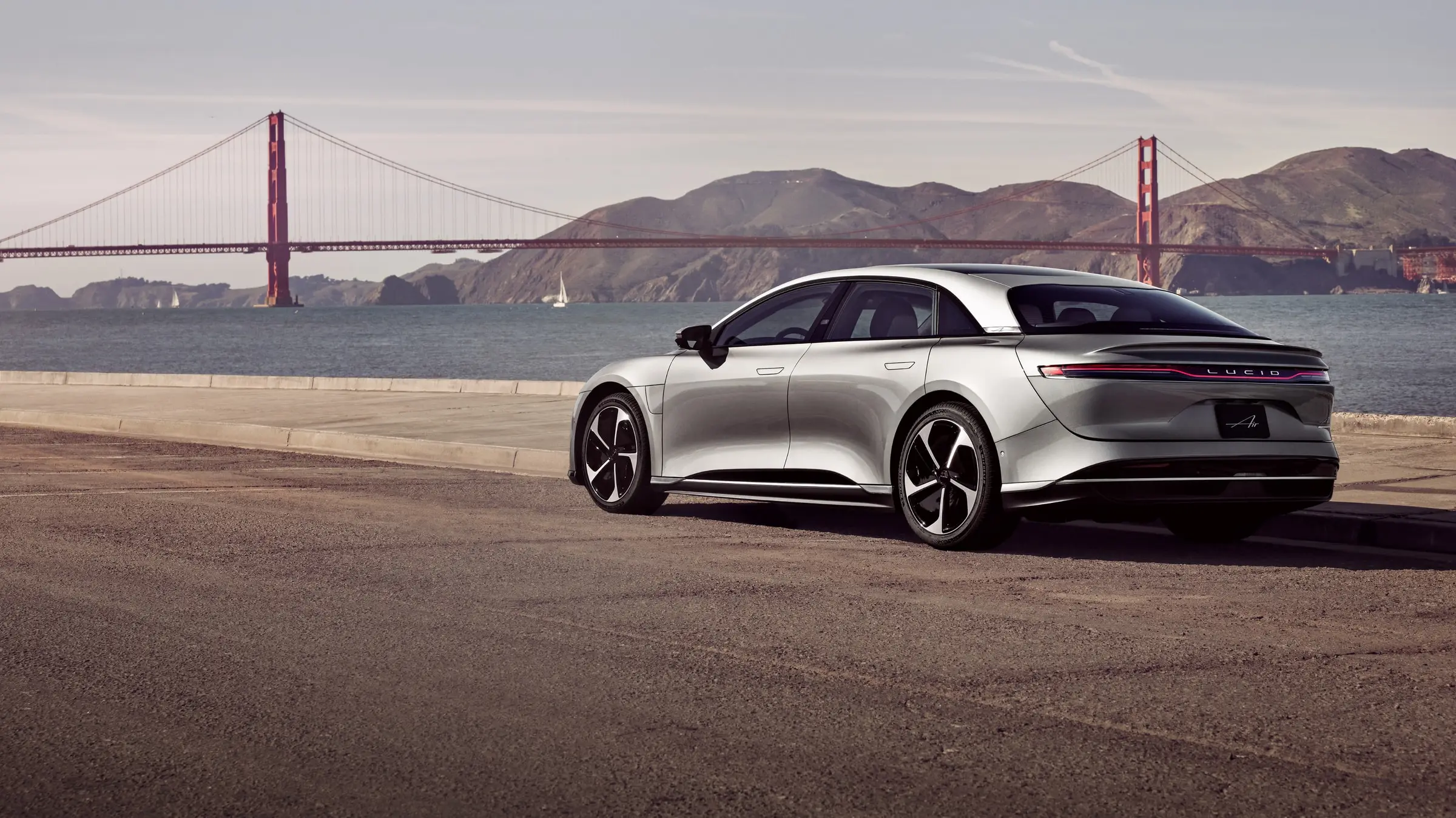 A silver Lucid Air Touring parked beside San Francisco Bay with the Golden Gate Bridge behind it